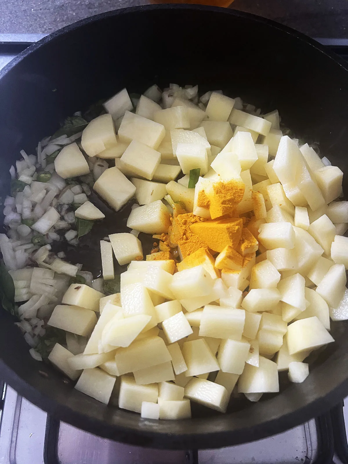 Adding the potatoes and ground turmeric to the pan.