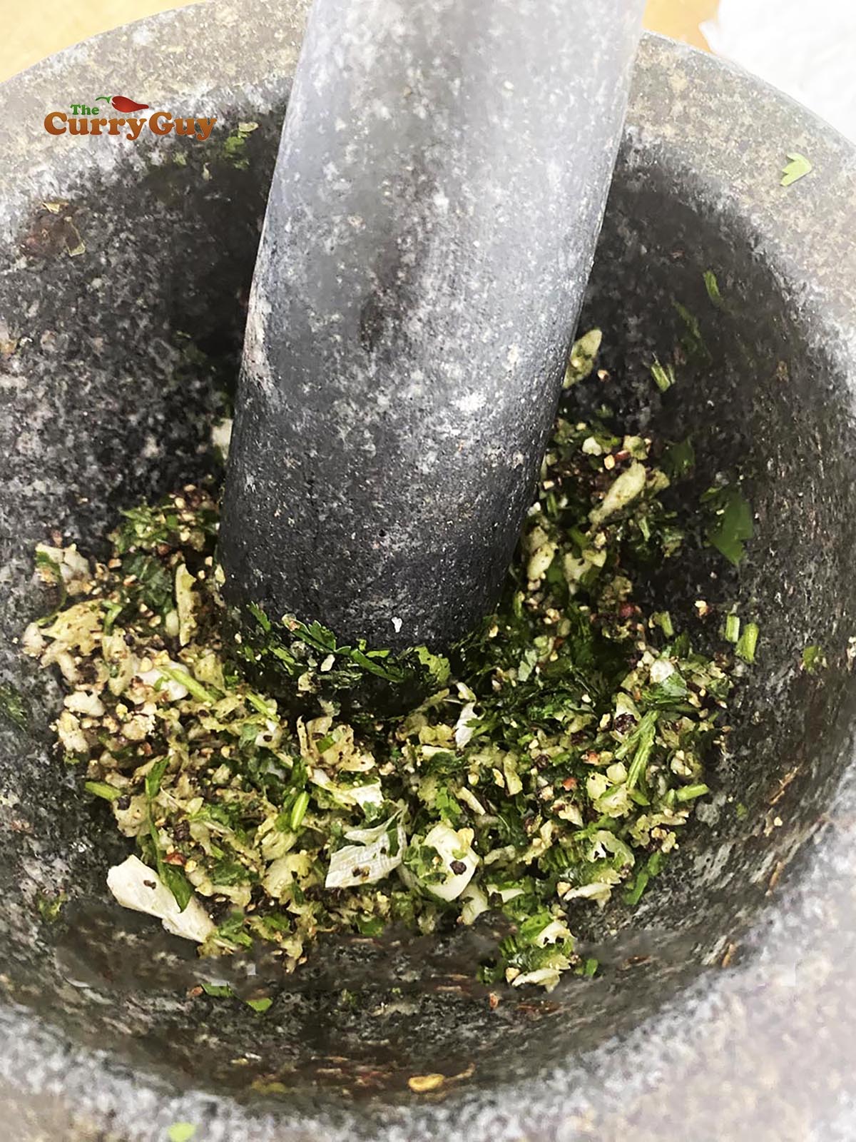 Smashing garlic and coriander in a pestle and mortar.