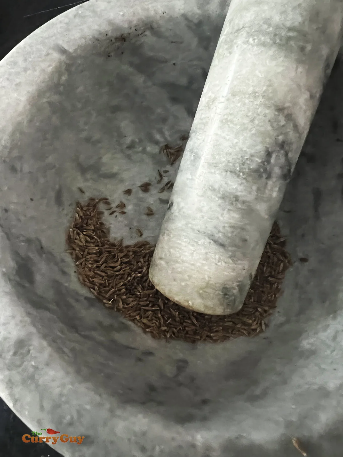 Pounding the cumin seeds in a pestle and mortar.