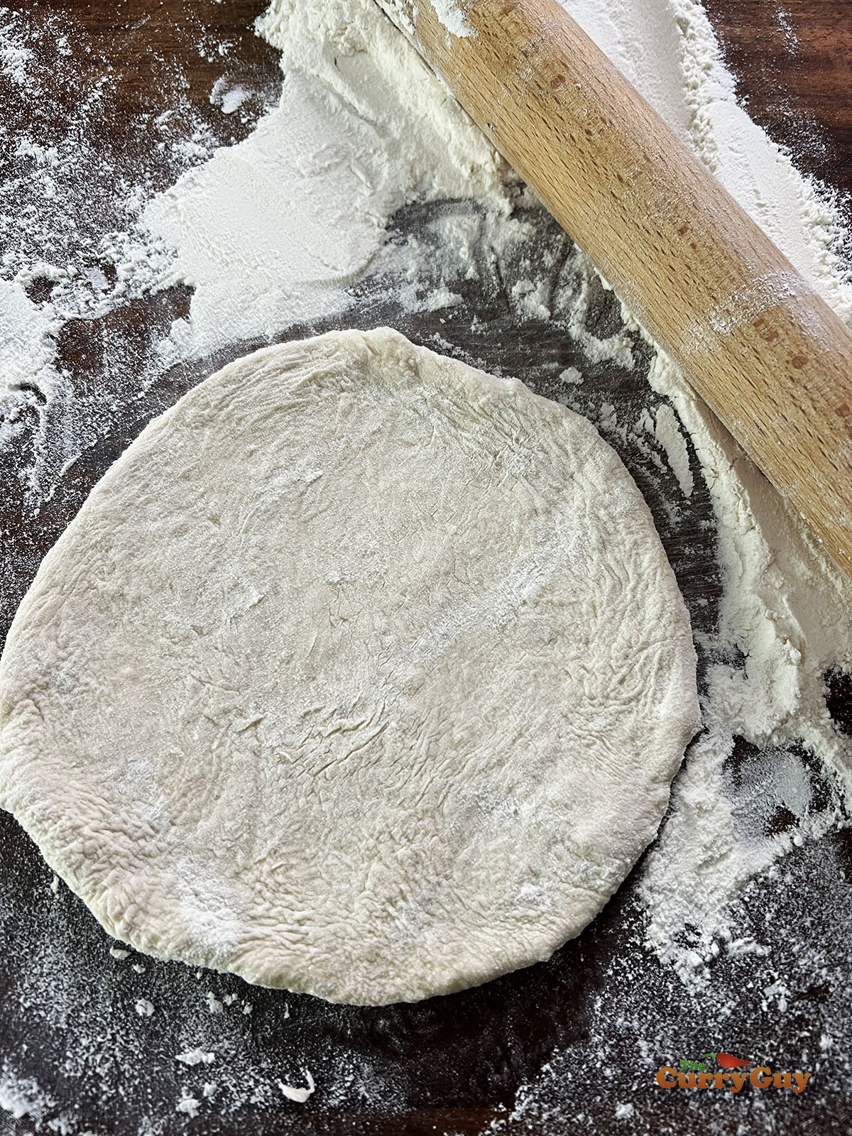 Rolling a dough ball into a round pita shape.