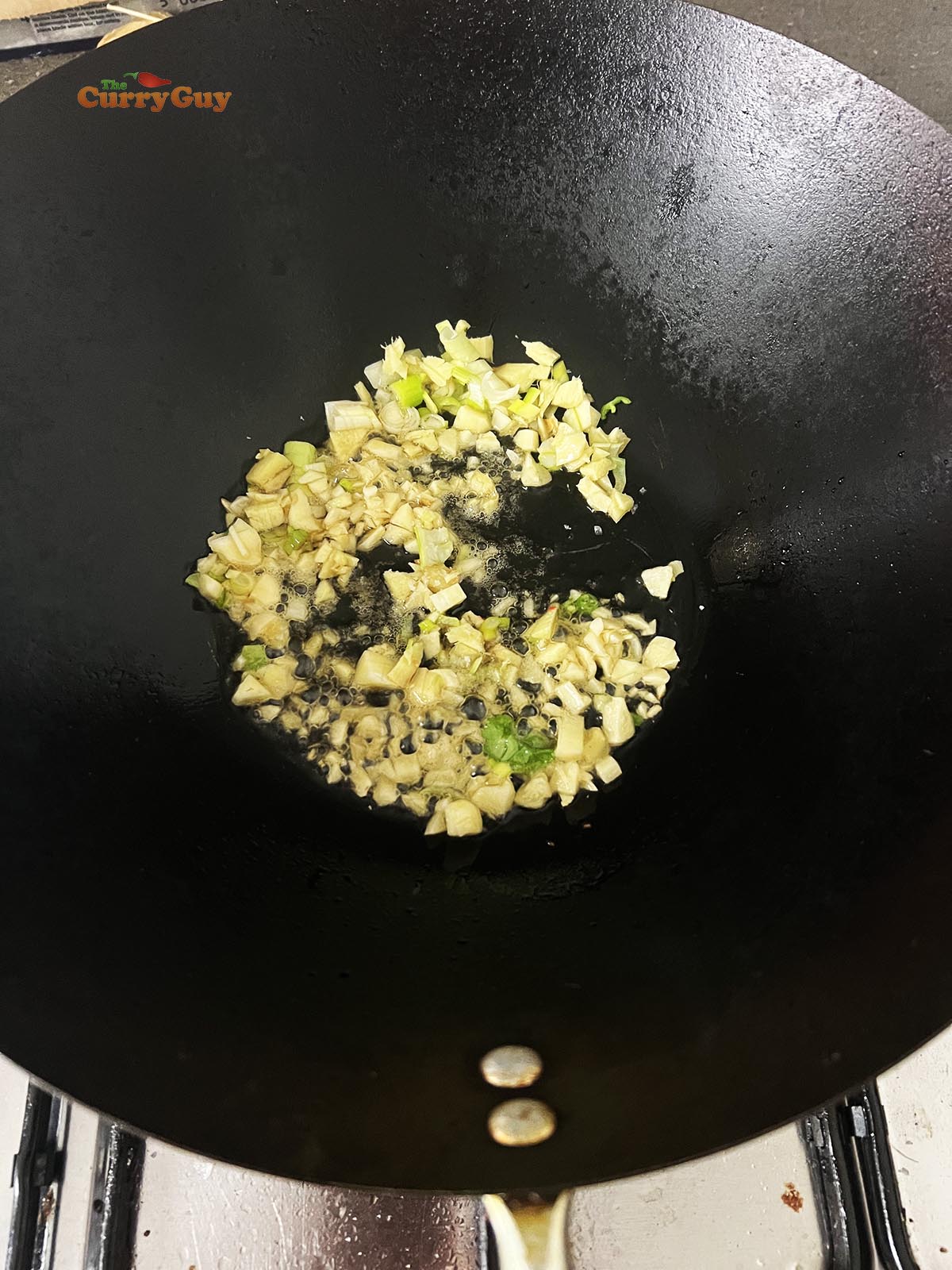 Frying the garlic, ginger and spring onions in a wok.