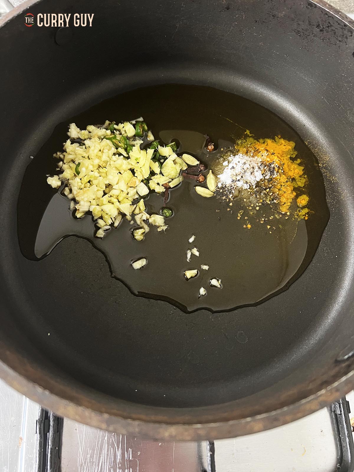 The oil heating in the pan with the garlic, cardamom, cloves, salt, sugar and ground turmeric.