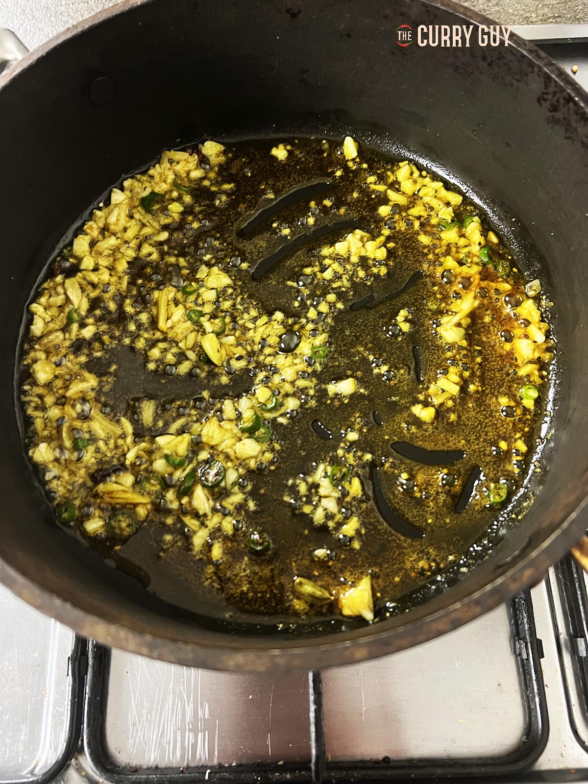 Stirring the garlic, cardamom, cloves, salt, sugar and ground turmeric into the oil.