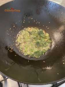 Adding curry leaves and cumin seeds to pan.