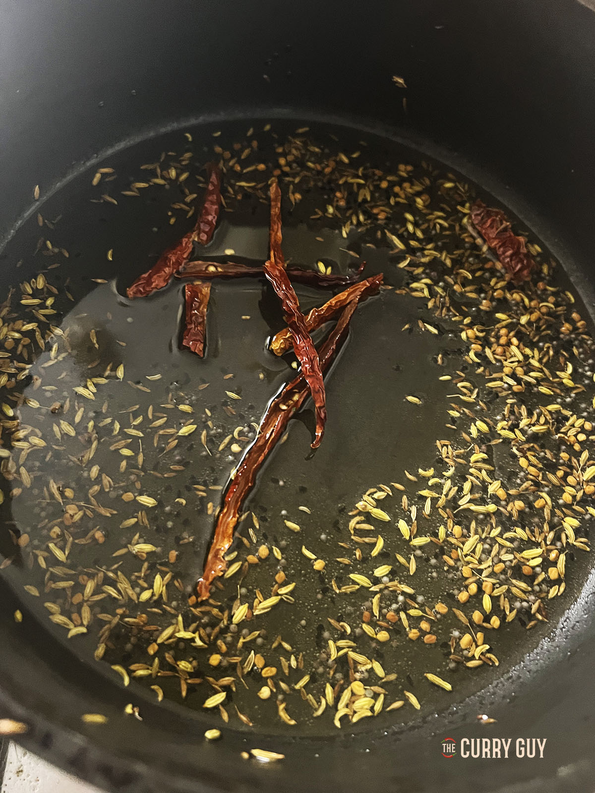 Tempering the spices and dried chillies in the oil in the pan.