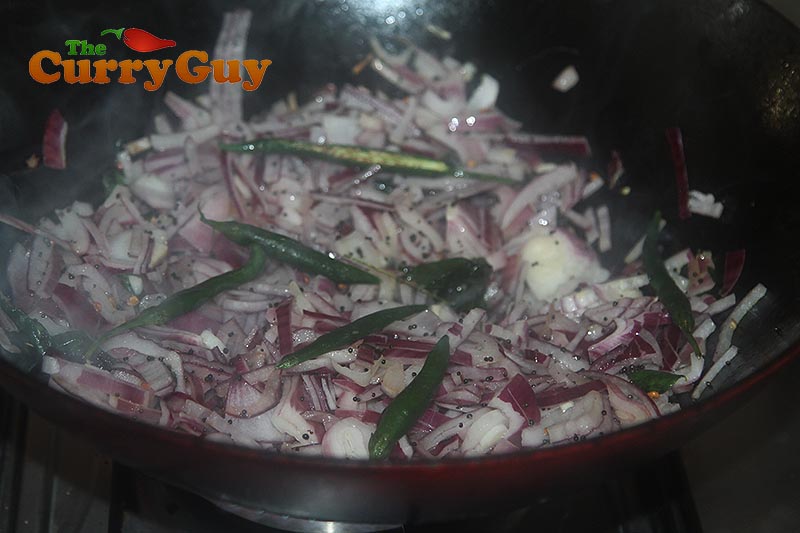 Adding onions and chillies to the spices and curry leaves.