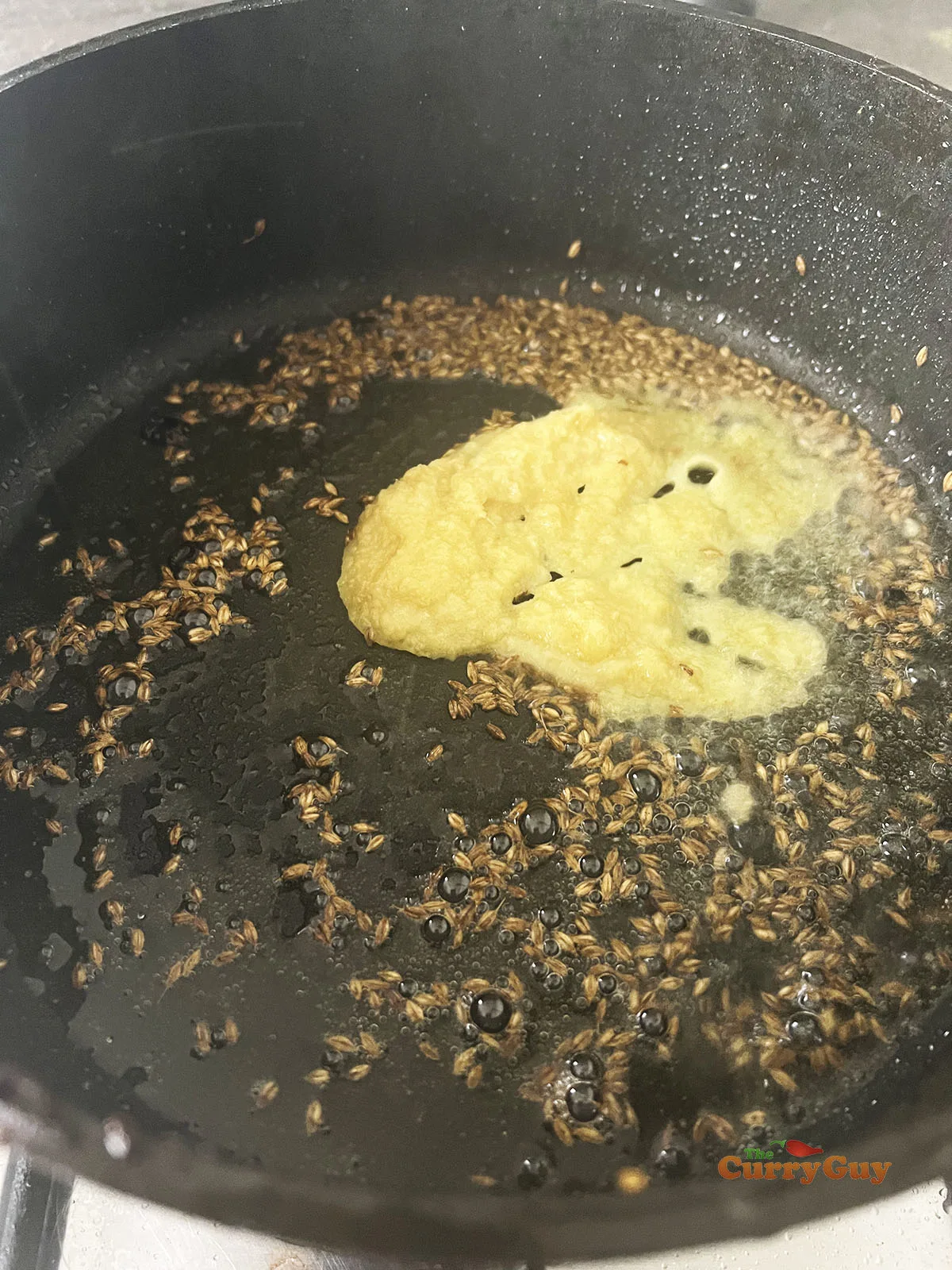 Adding cumin seeds and garlic and ginger paste to the pan.