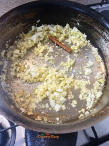 Adding cinnamon stick and chopped onion to pan