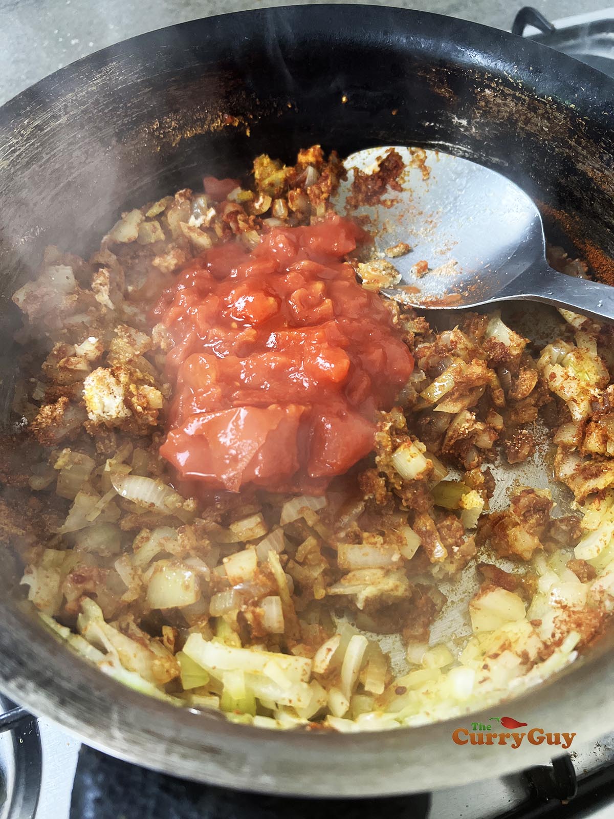 Adding spices and tomatoes to the frying pan