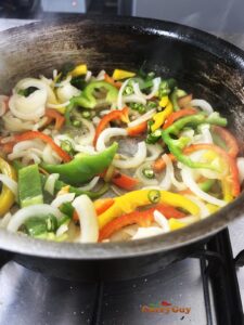 Stirring sliced onions and bell pepper to the pan