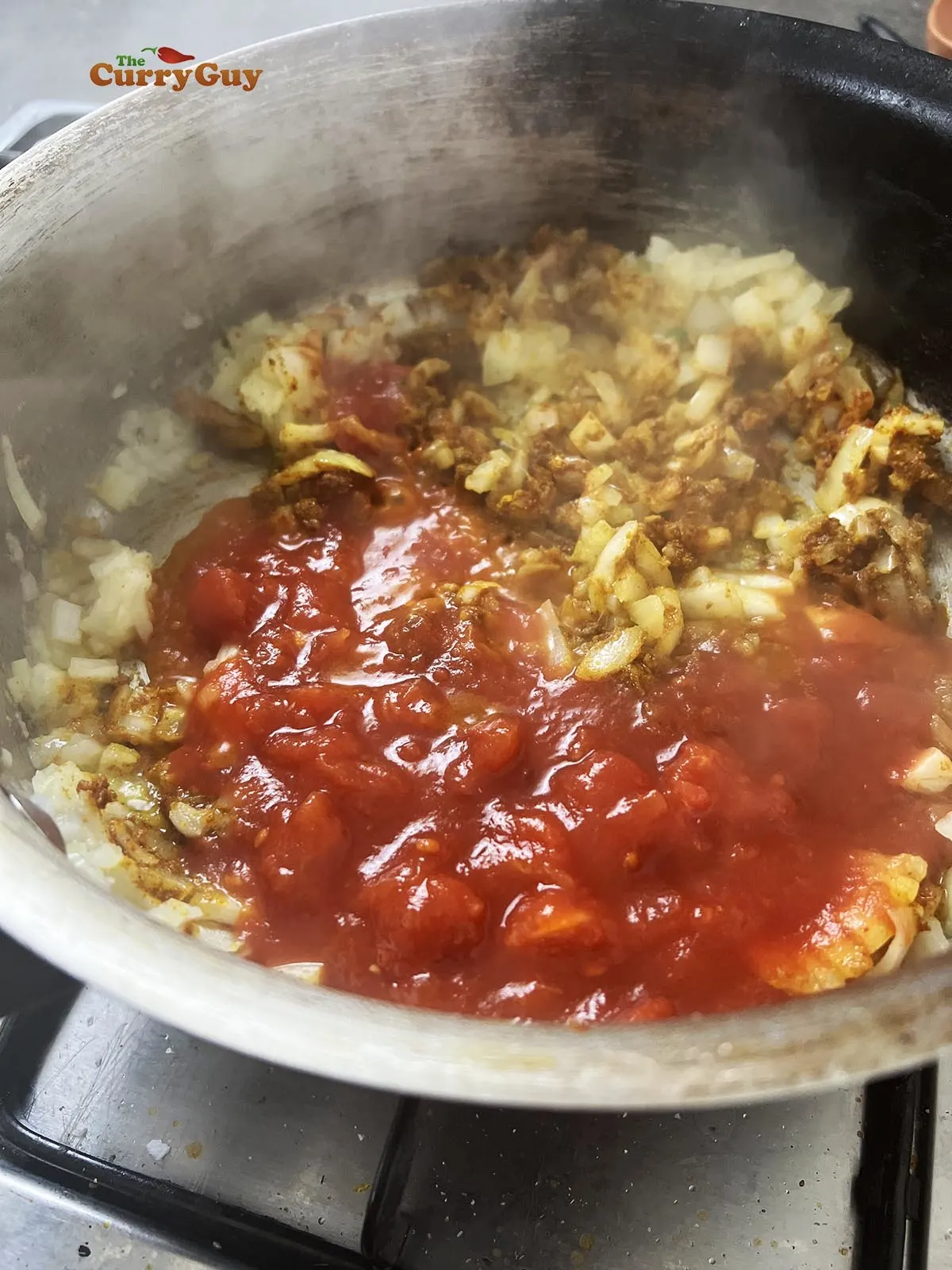 Adding ground spices and chopped tomatoes to the pan