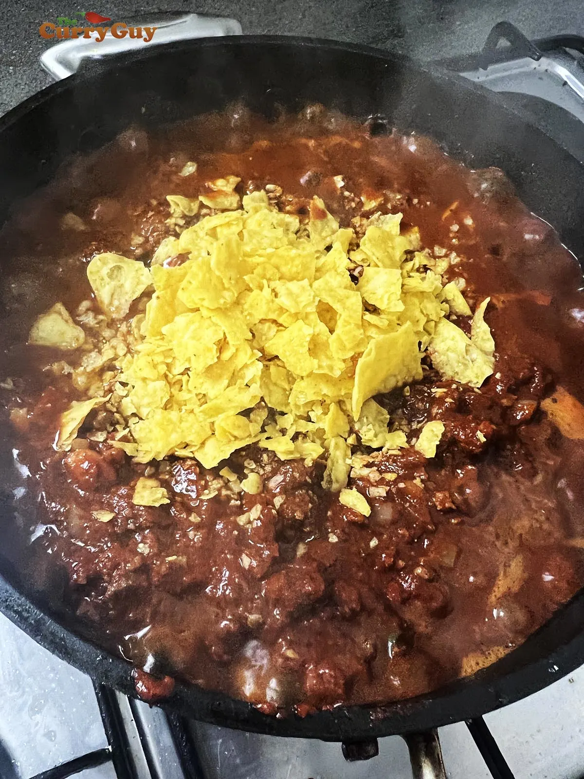 Adding corn chips to the chili con carne.