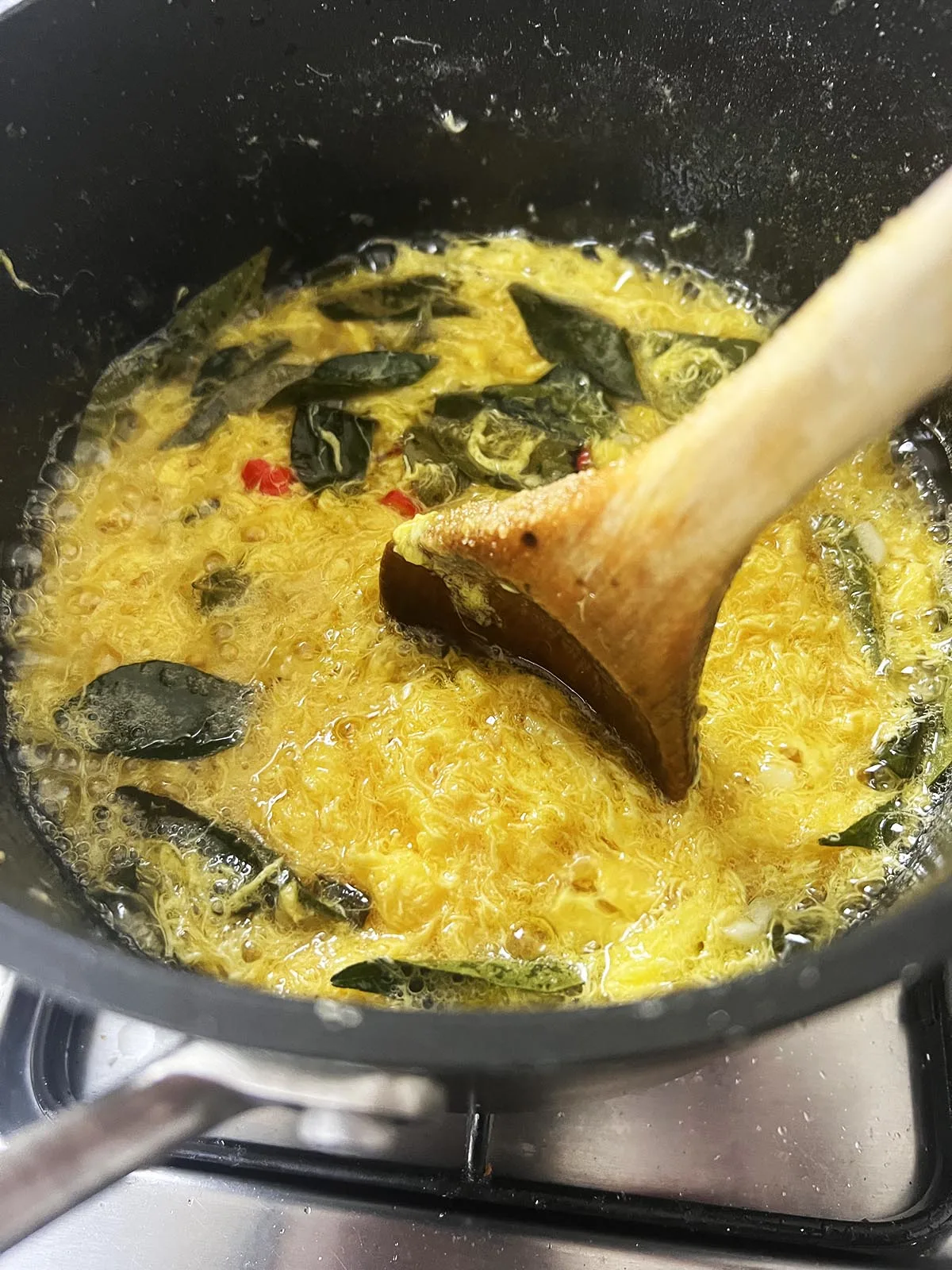 Stirring curry leaves and chillies into the egg yolk mixture.