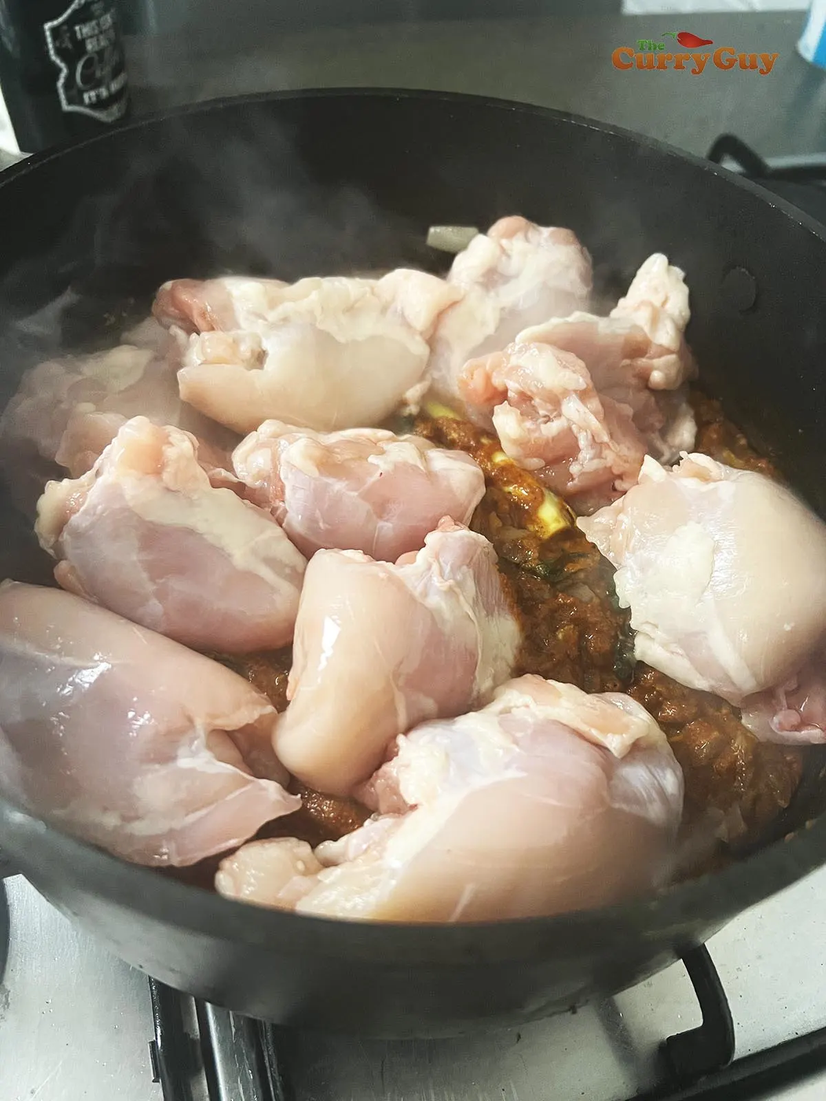 Adding the spice pastes and chicken to the pan.