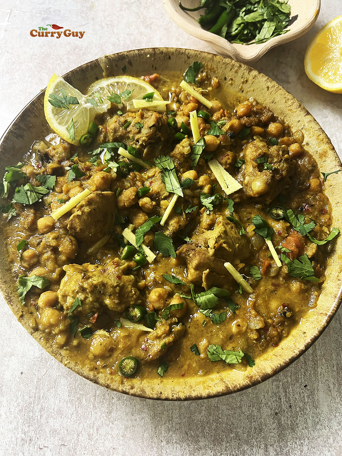 Chicken and chickpea curry garnished with lemon, chillies, coriander (cilantro) and julienned ginger. 