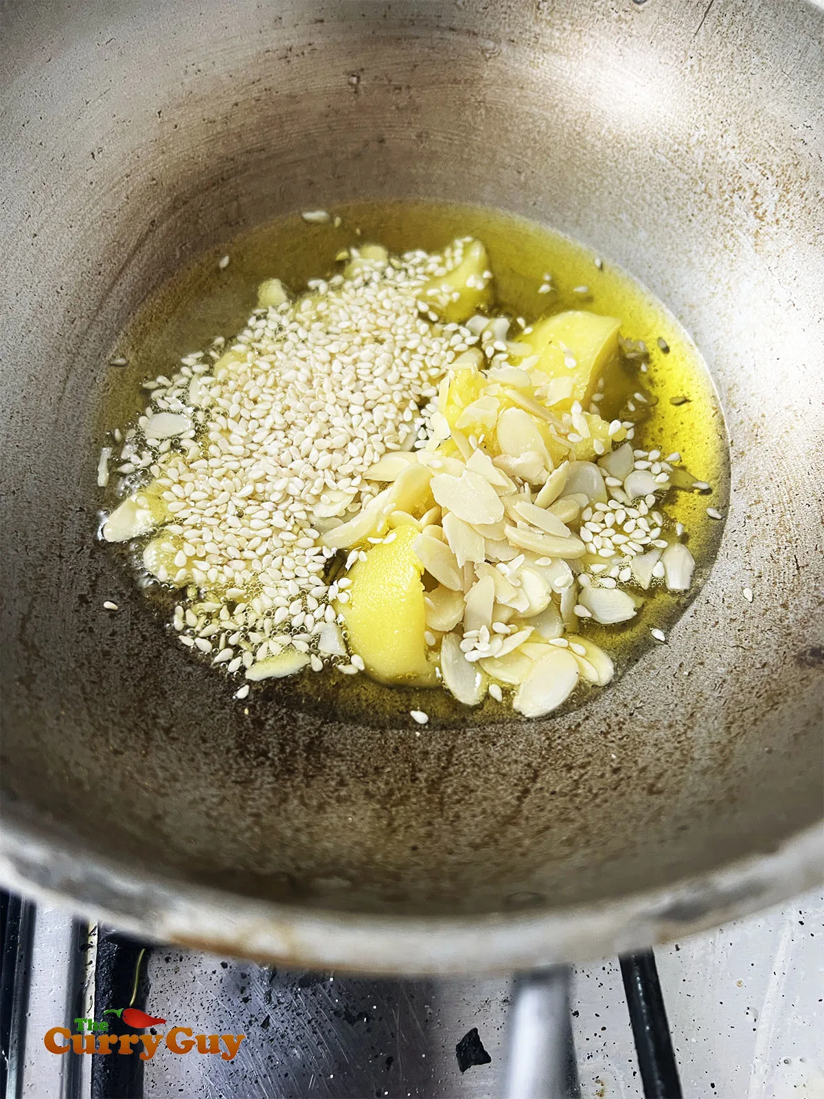 Toasting almond flakes and sesame seeds in hot ghee.