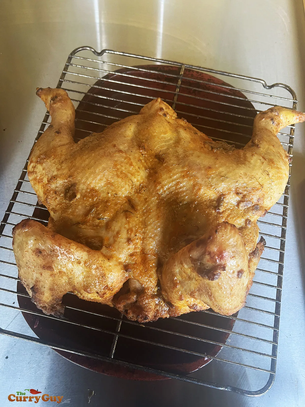Half cooked chicken on a metal rack, drying and dripping.
