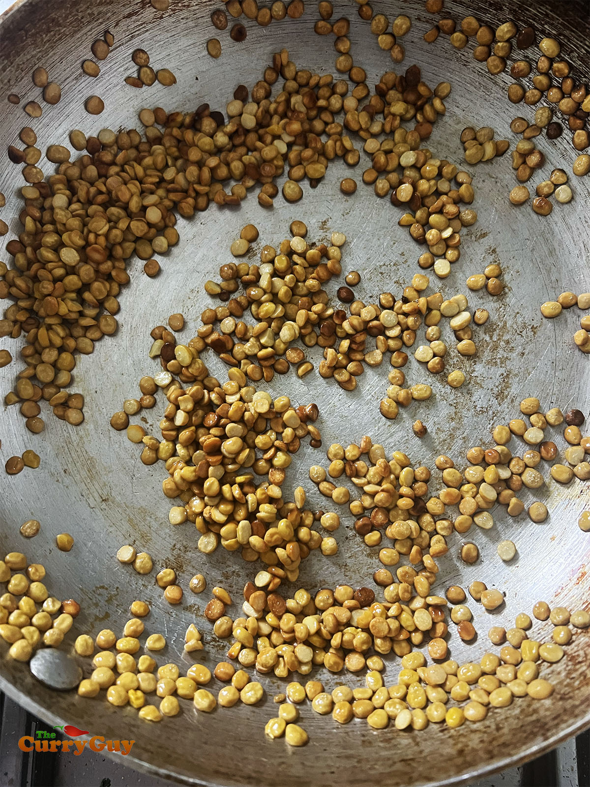 Toasting chana lentils in the pan until golden brown.