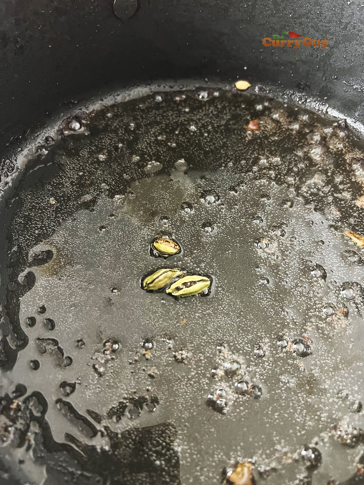 Infusing caramom pods in oil in a pan.