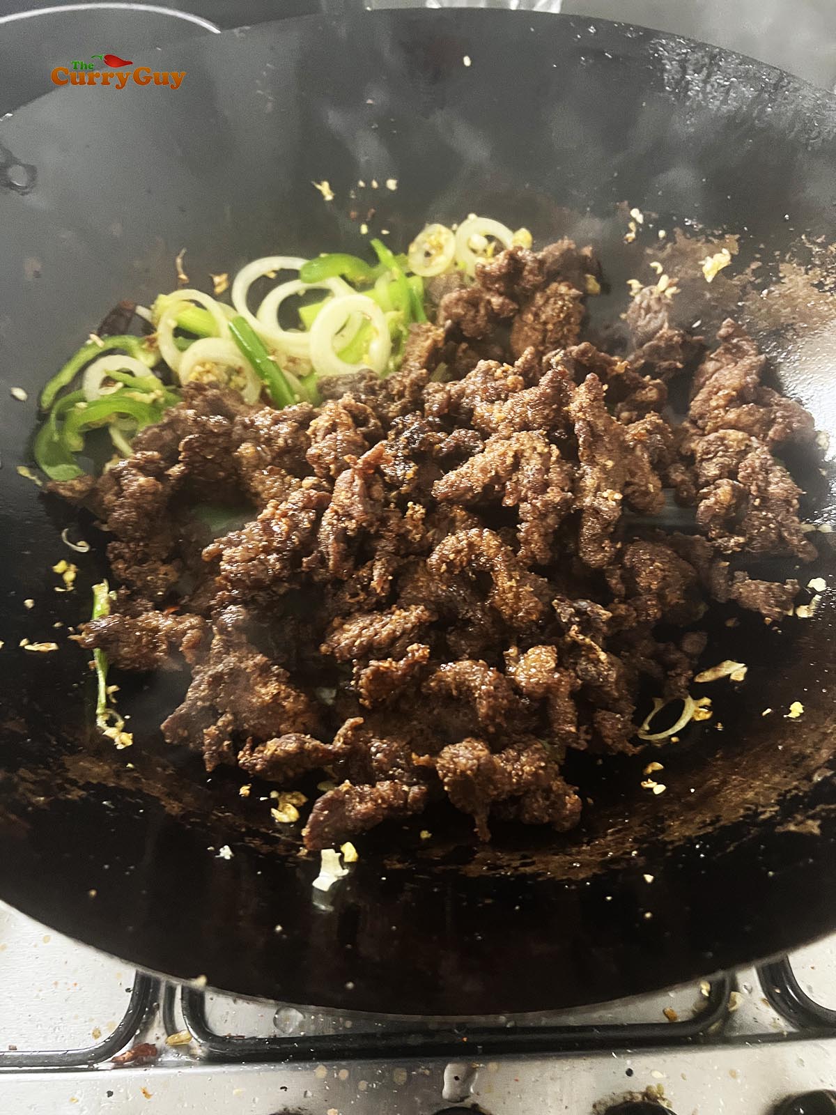 Adding the fried beef and sauce to the wok.