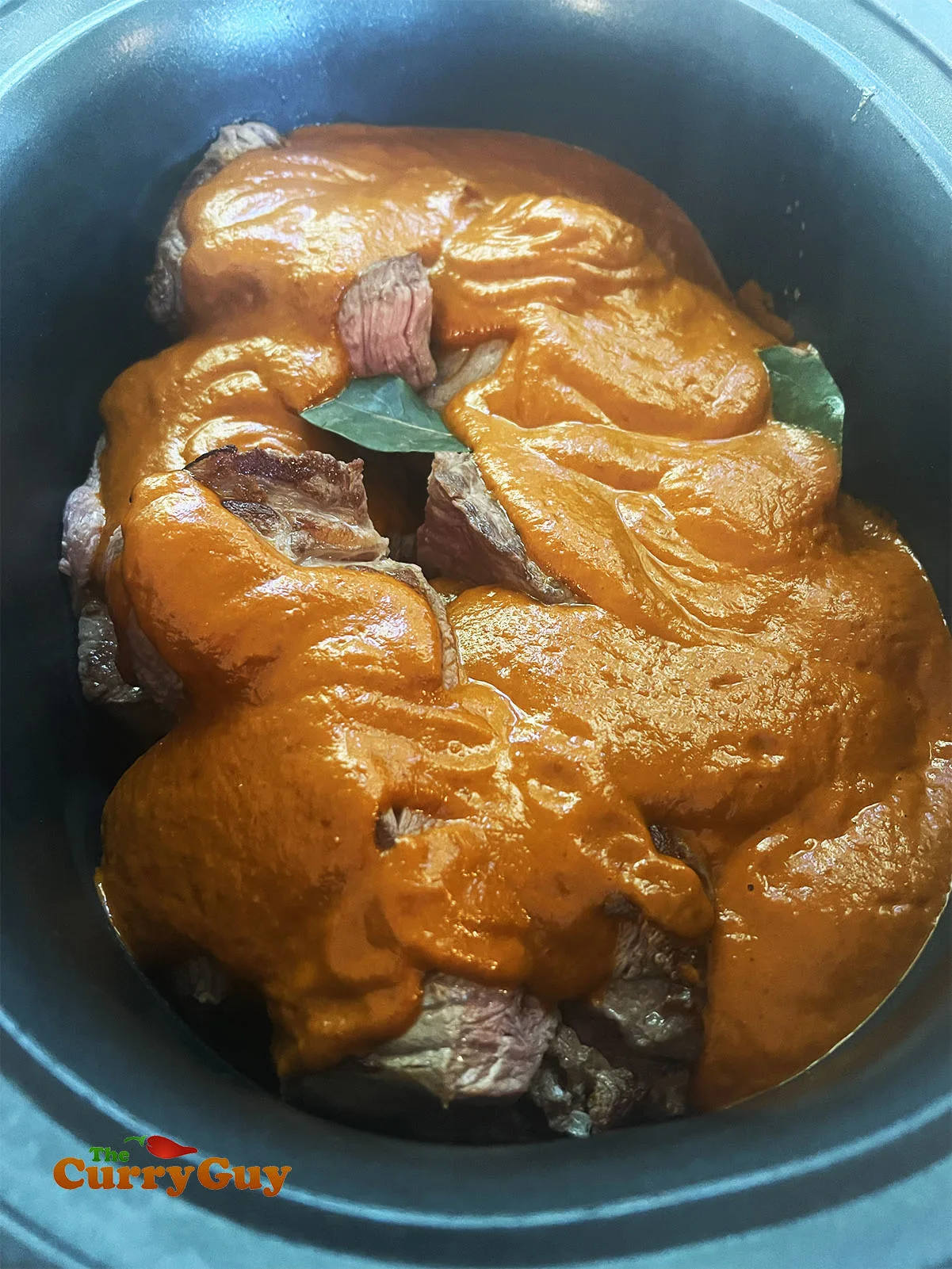 The meat in a pan covered with the paste and stock.