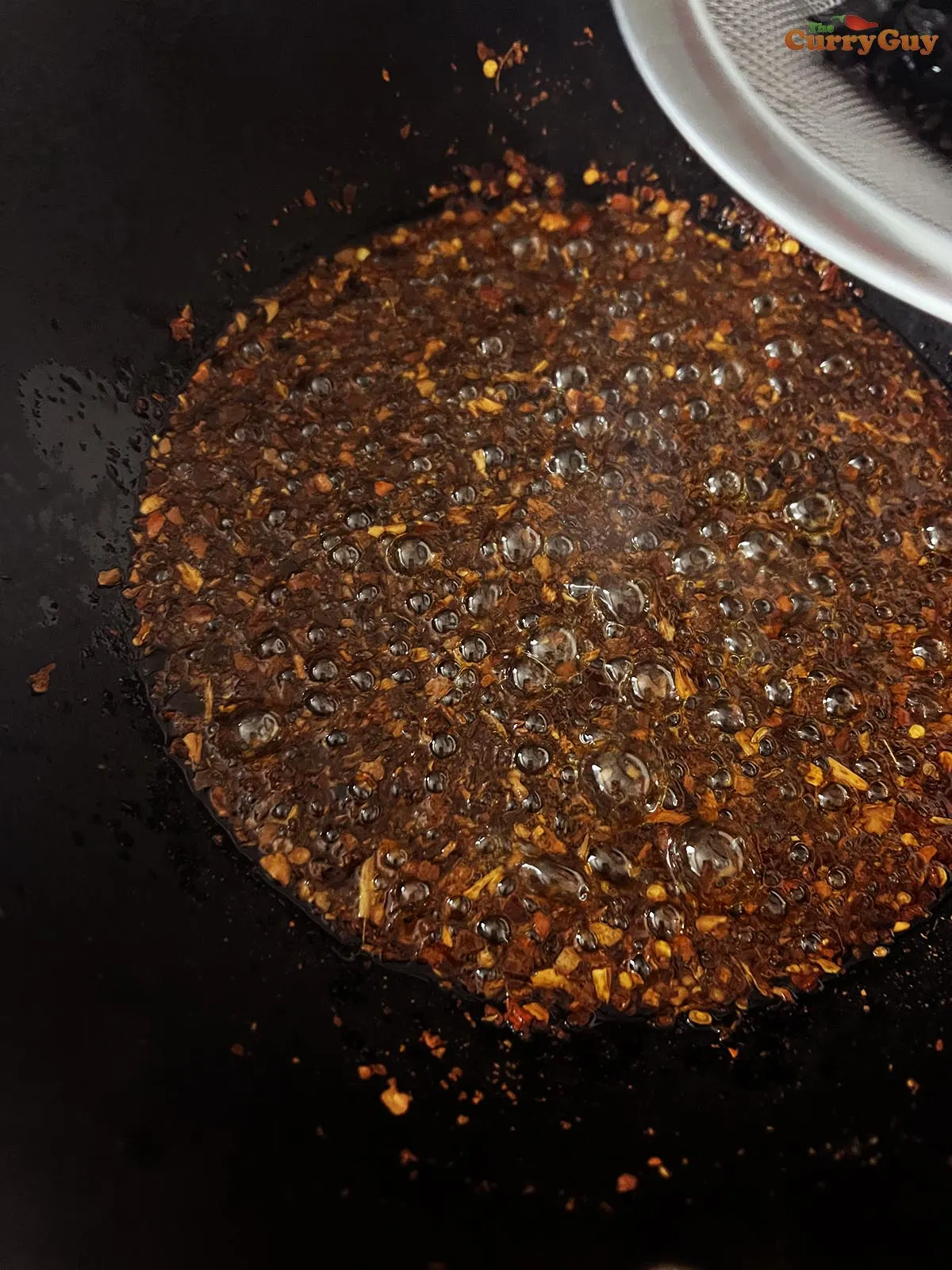 Pouring the spice infused oil through a sieve over the chili flakes.