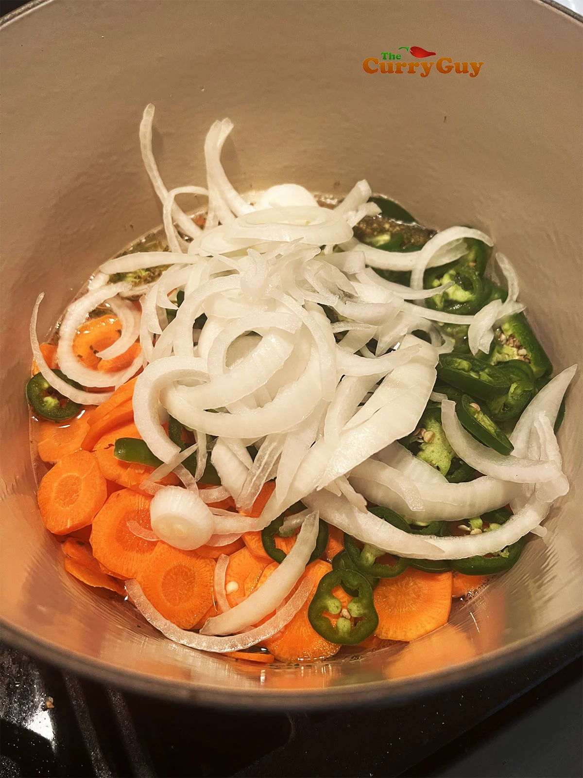 Adding carrots, onions and chilies to the boiling water and vinegar.