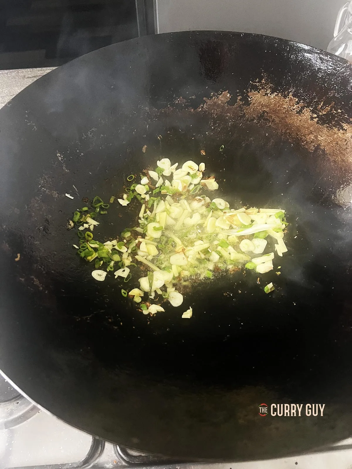 Frying the garlic, ginger and spring onions (scallions) in a wok.