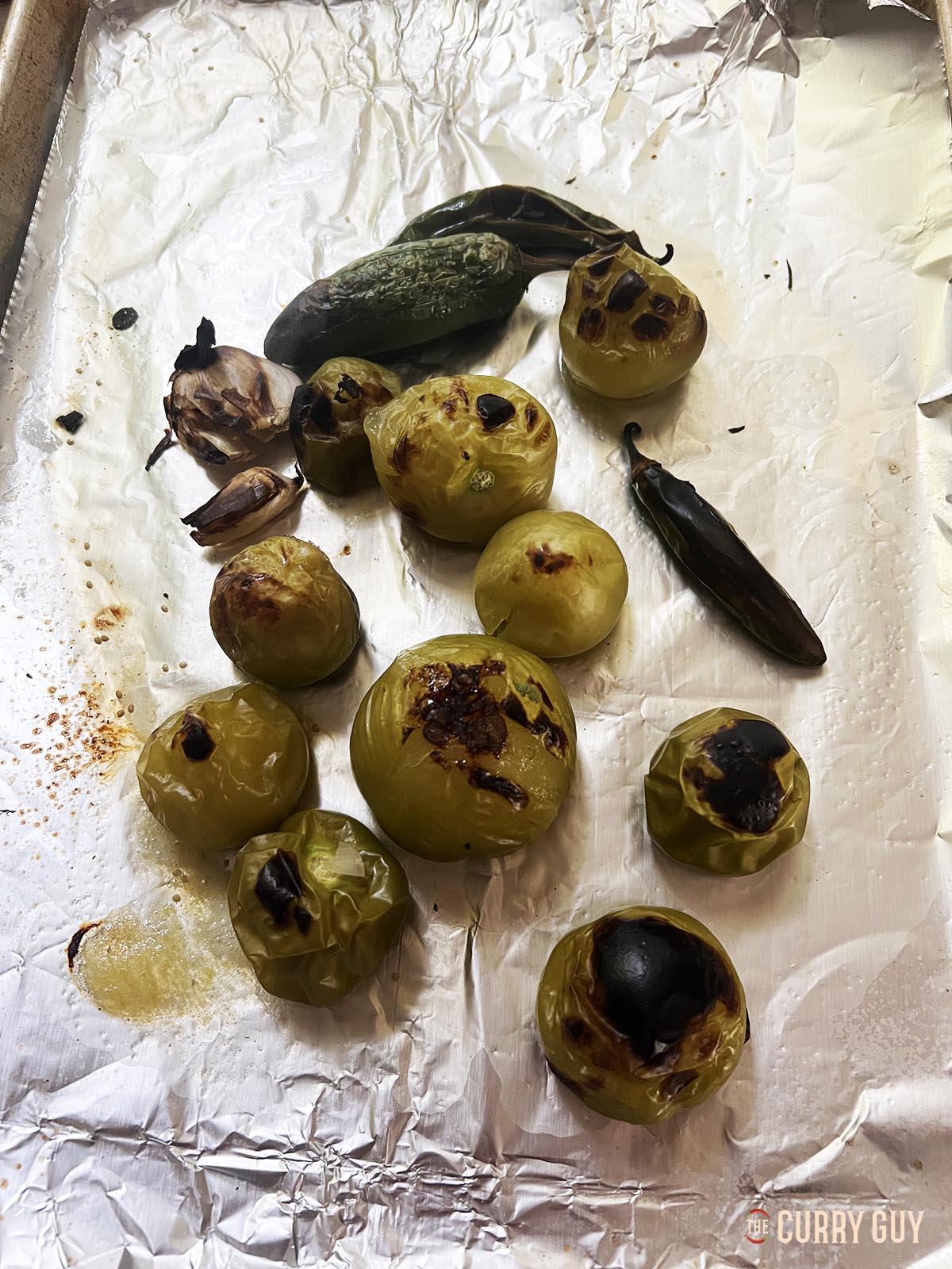The roasted tomatillos, chilies and garlic on a baking tray.