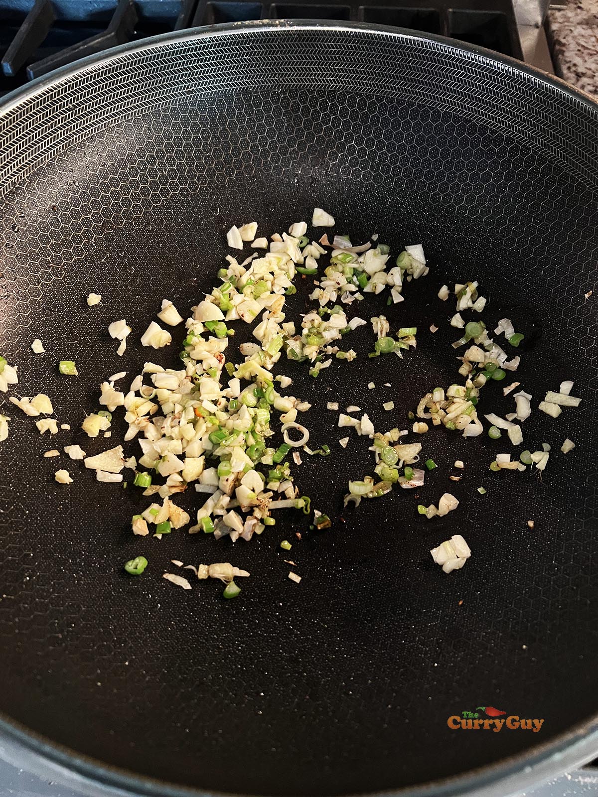 Frying the chopped garlic, ginger and spring onions (scallions) in a hot wok.