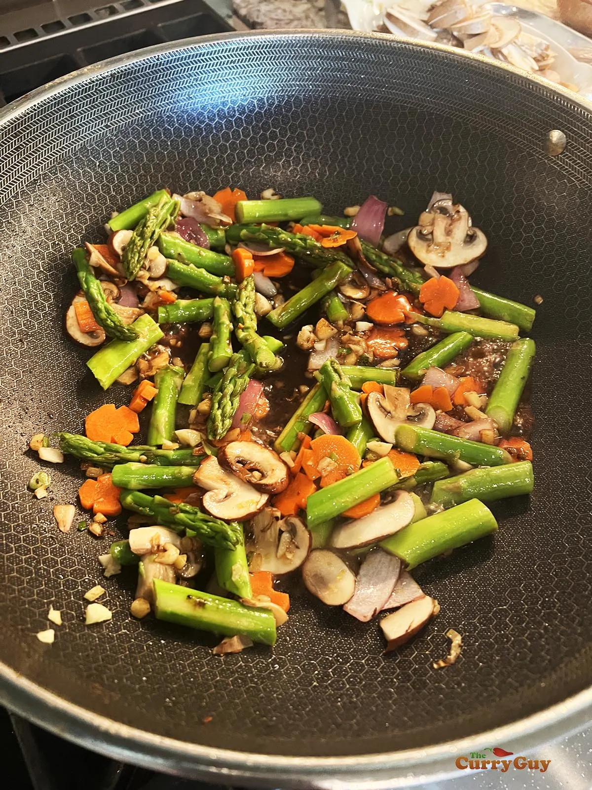 Returning the blanched carrots and asparagus to the wok.