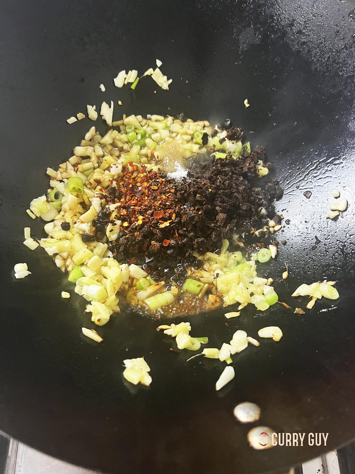 Adding the black beans and dried chilli flakes to the wok.