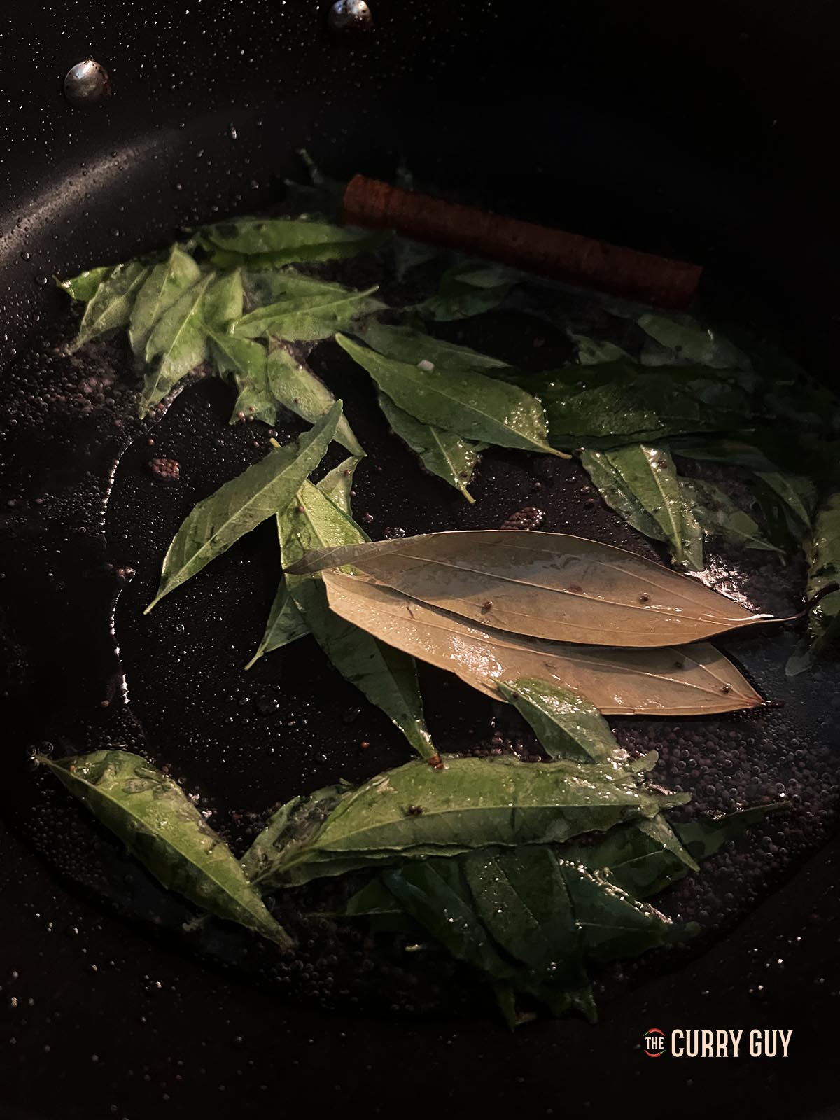 Adding the curry leaves and bay leaves to the hot coconut oil. 