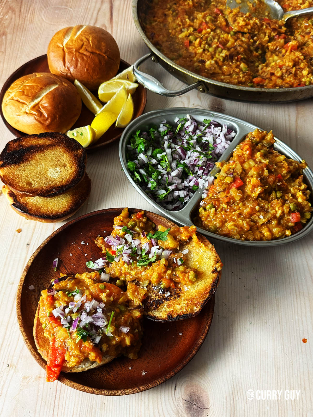 Pav bhaji on a serving plate garnished with chopped red onion and coriander. 