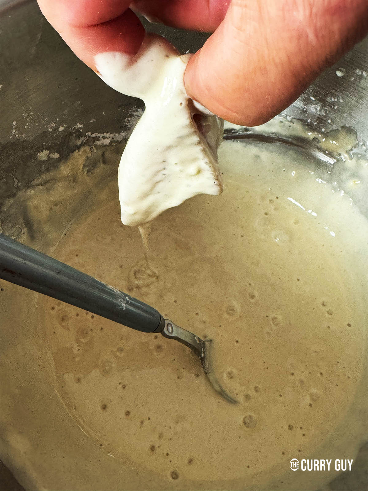 Dipping a piece of chicken into the prepared batter.