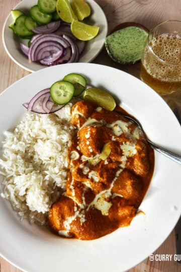 Butter chicken in a serving bowl with rice and a side of cucumber and red onion.