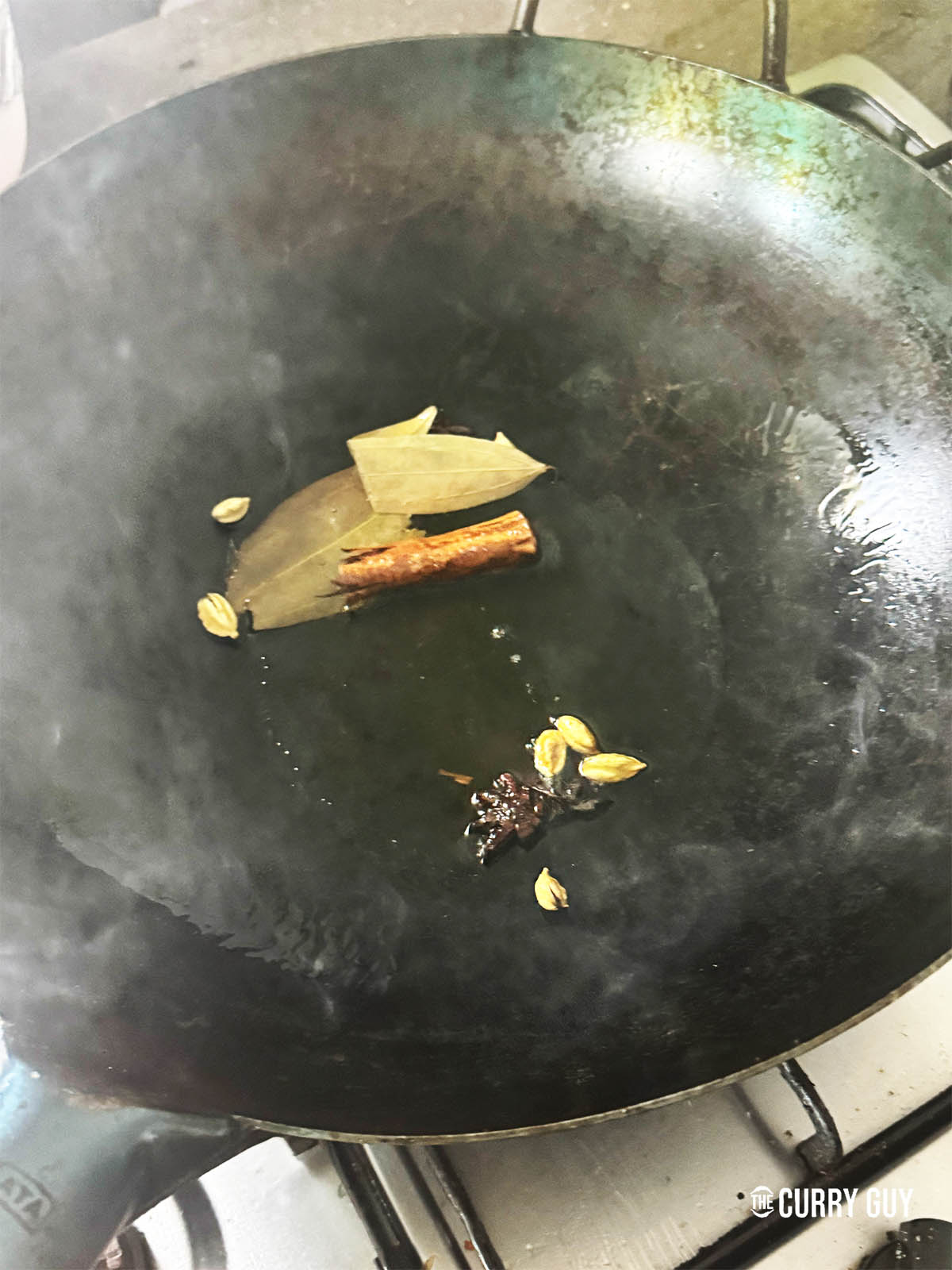 Adding the whole spices to ghee in the pan.