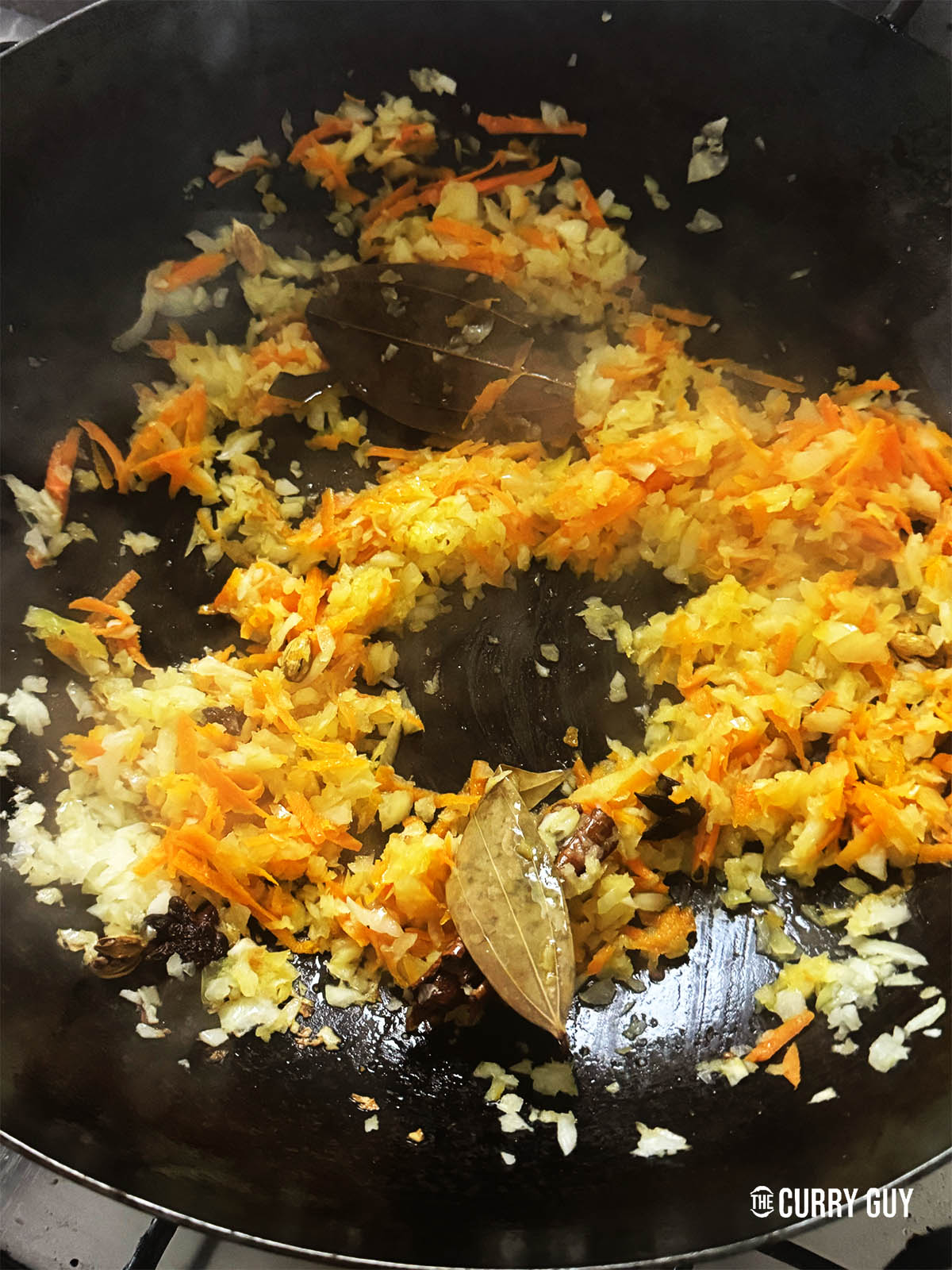 Adding the chopped onions and carrot to fry with the spices in the ghee.