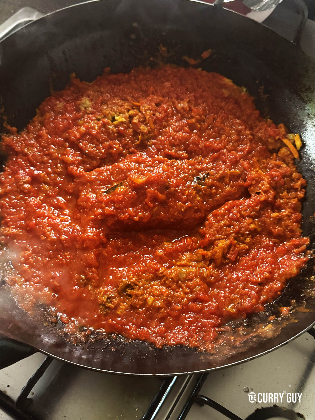 Adding the ground spices and stirring the curry together in the pan.