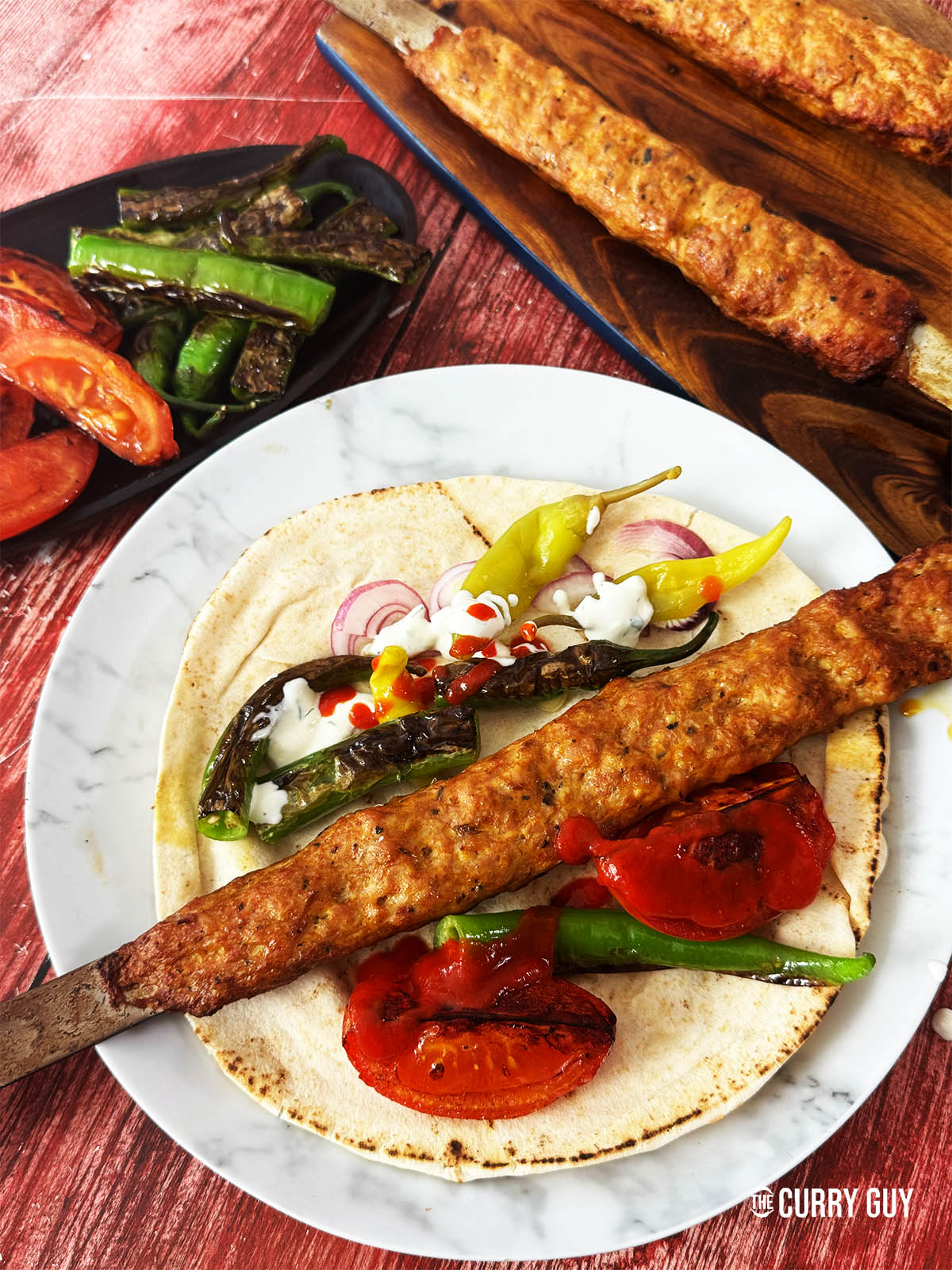 The finished chicken koobideh on a serving plate on a flatbread with salad vegetables and sauces.