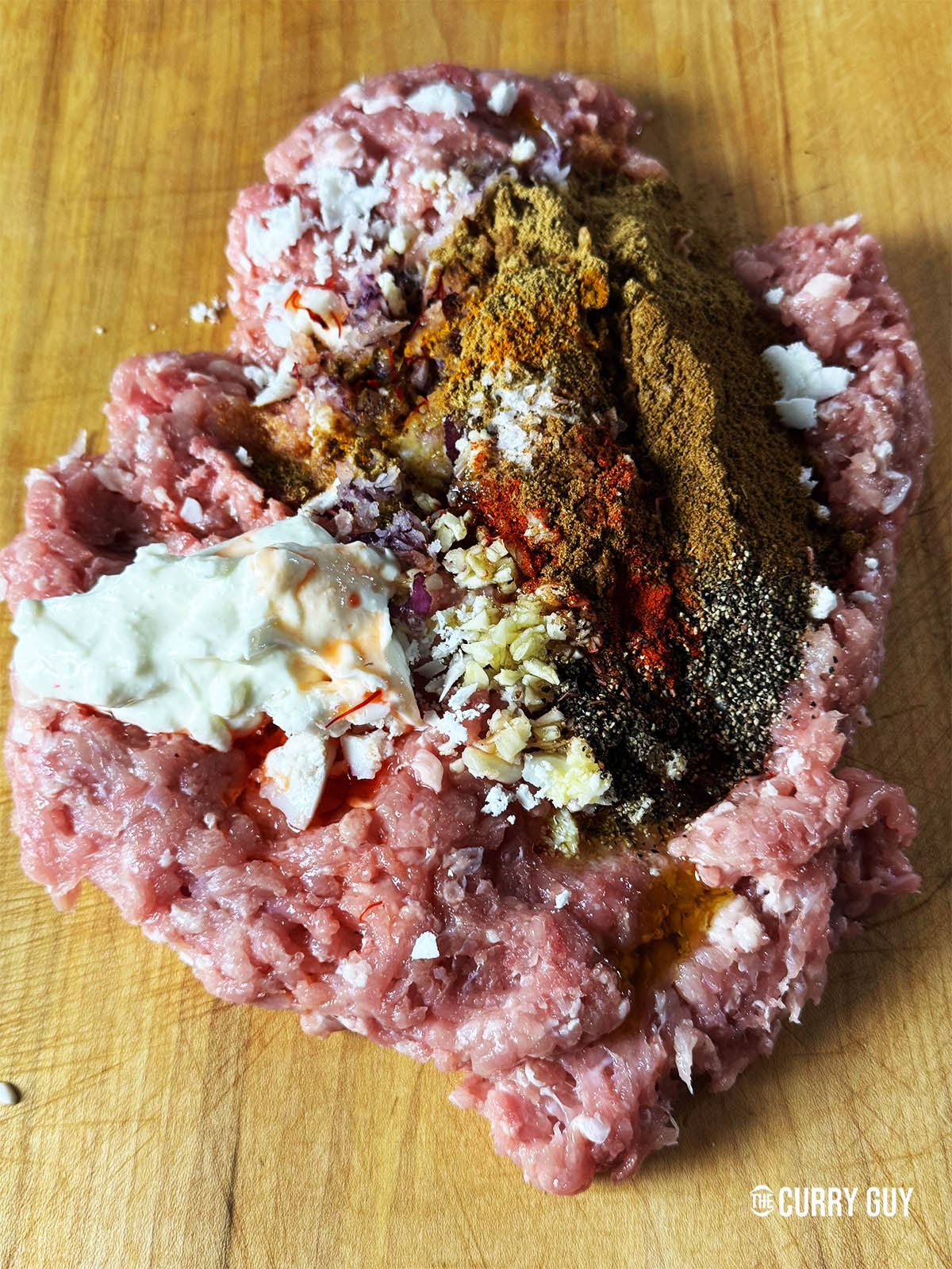 The minced chicken, lamb fat, salt pepper, garlic and ground spices on a counter top ready to knead.