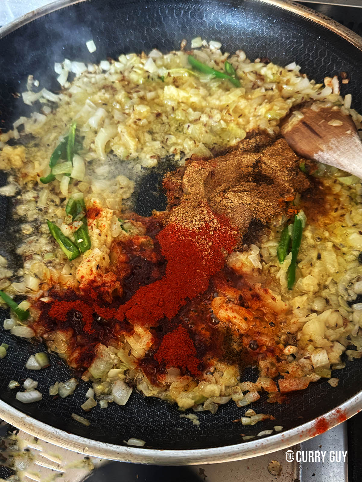 Adding ground chillies to the fried onion mixture in the pan.