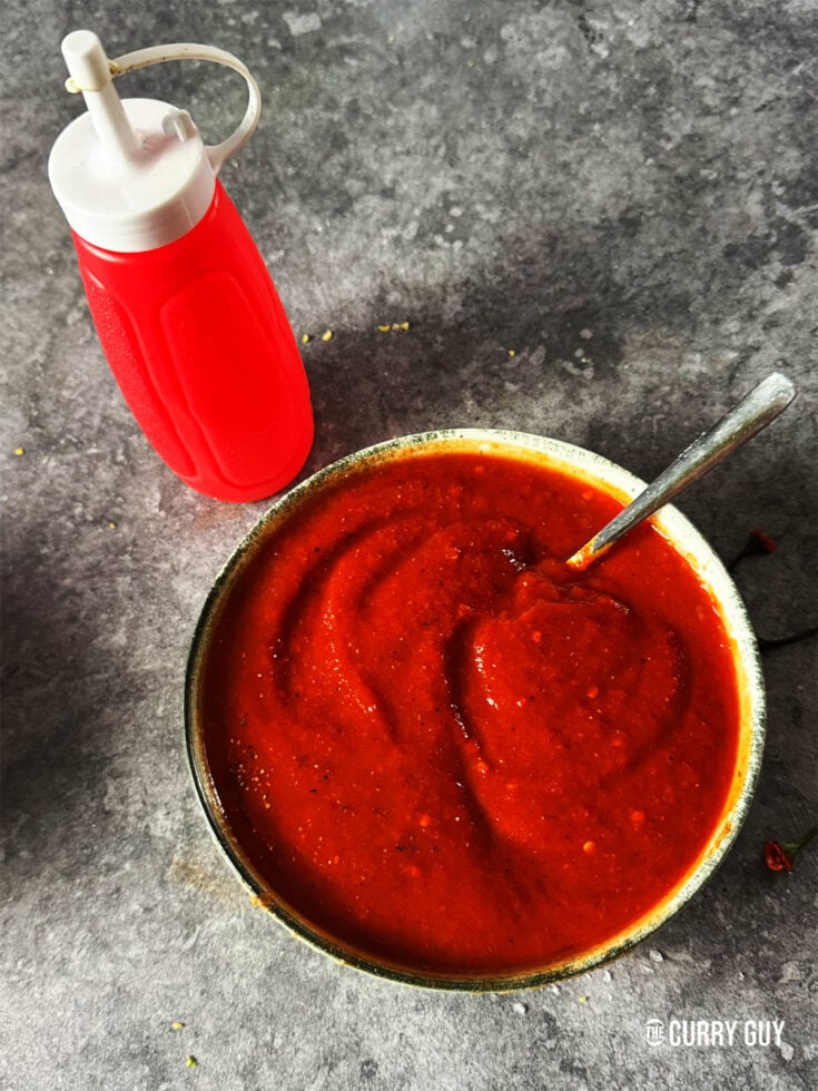 Red kebab shop sauce in a serving bowl next to a squeeze bottle.