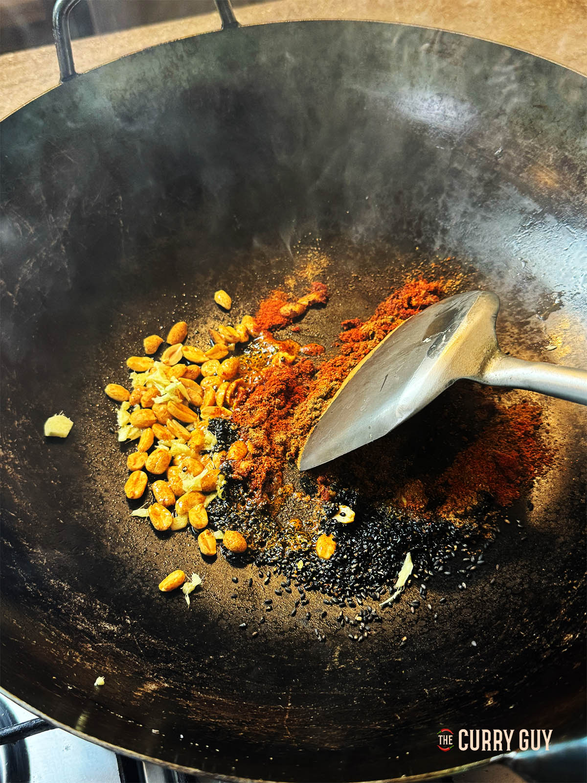 Adding the ground spices, peanuts and poppy seed to the oil in the wok.