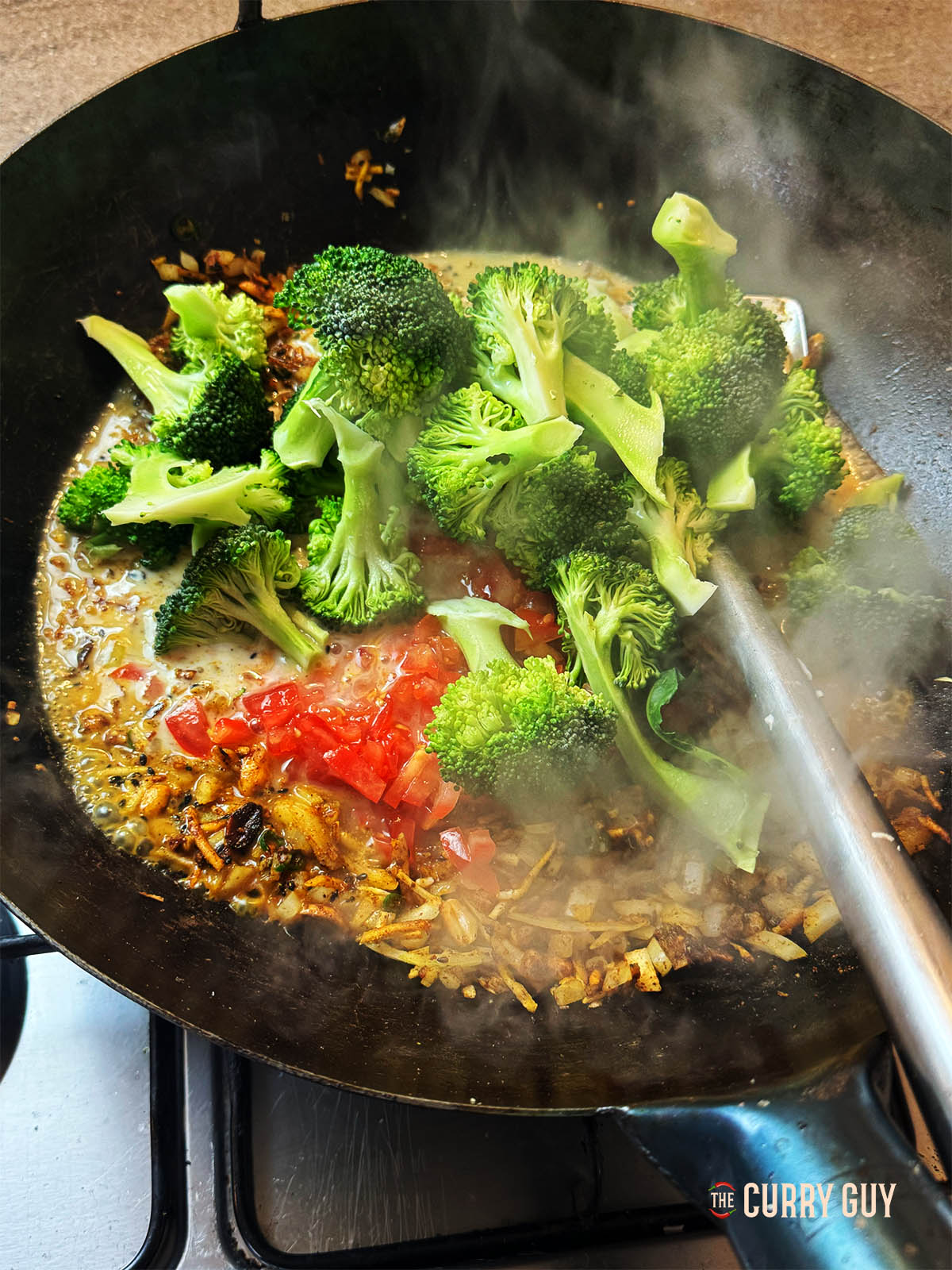 Adding the broccoli, coconut milk and chopped tomatoes to the pan.