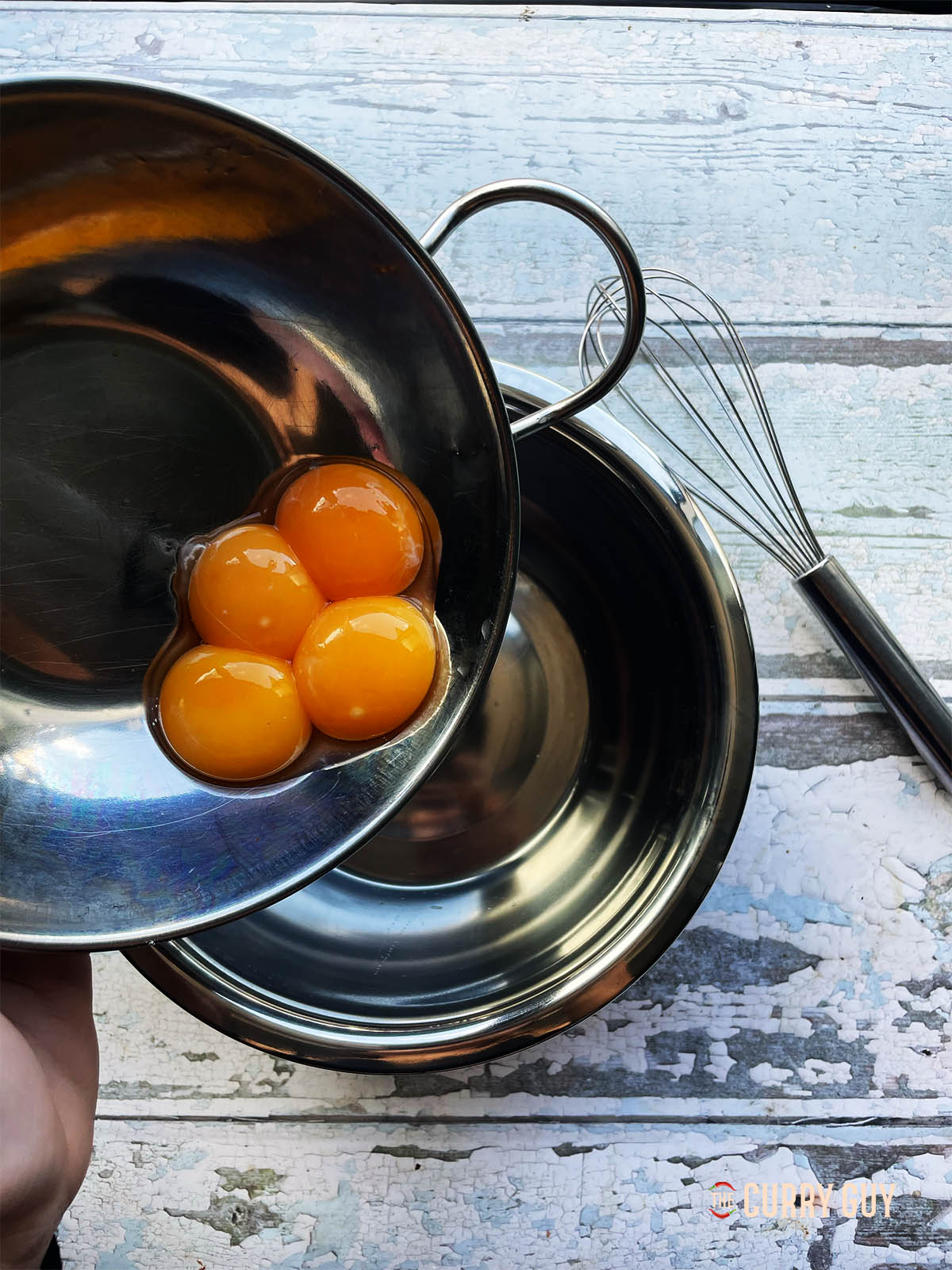 4 egg yolks being poured into a mixing bowl.