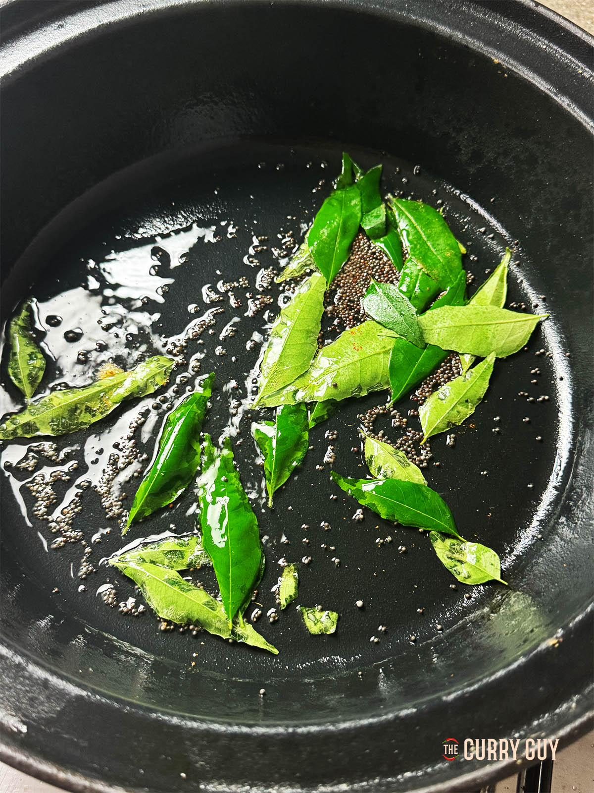 The mustard seeds and curry leaves infusing into coconut oil in a pan. 