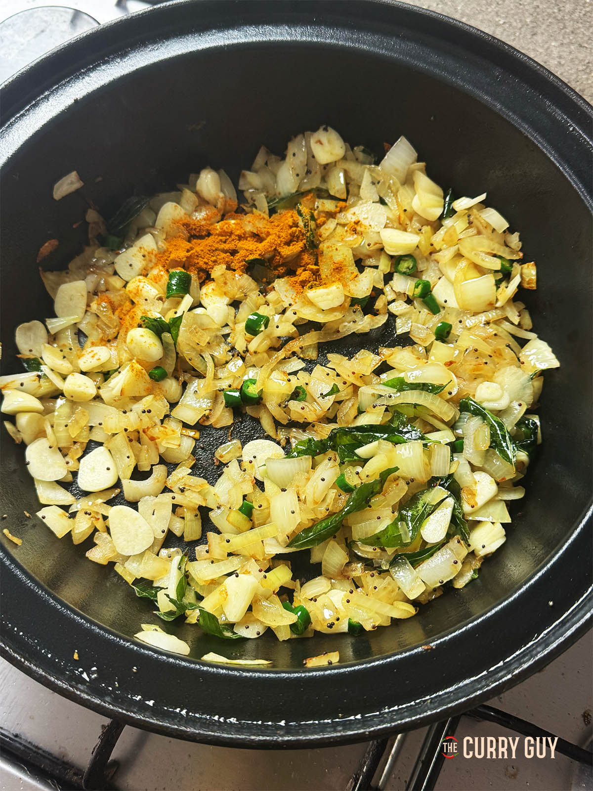Adding the sliced garlic, chillies and ground turmeric to the pan.