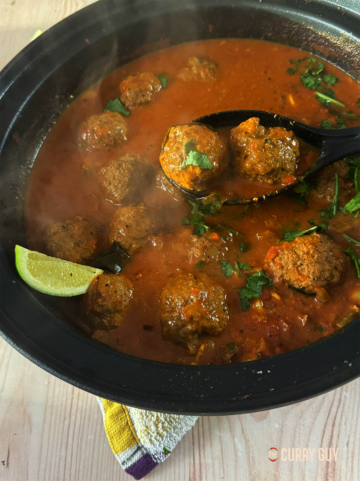 Two koftas in a spoon with the curry in the background. 