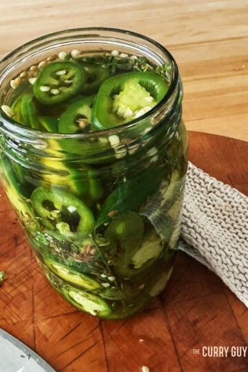 Pickled jalapeños in a preserve jar with the lid off.